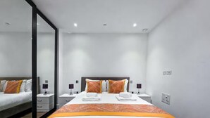 Moderni hotellihuone, jossa on suuri sänky, kaksi yöpöytää, peili ja pieni sivupöytä.