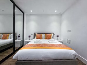 A modern hotel room with a large bed, two bedside tables, a mirror, and a nightstand. - Sleek flat near the City 5 min from station - Pass the Keys (London)