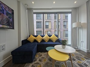 A modern living room with a sectional sofa, a small round table, and a potted plant. - Sleek flat near the City 5 min from station - Pass the Keys (London)