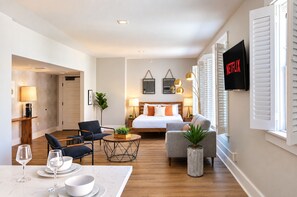 A modern hotel room with a bed, seating area, dining table, and a TV mounted on the wall. - The Penn Hotel - King Bed, AC & Gaslamp Nightlife! (San Diego)