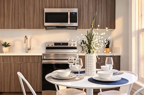 Una cocina moderna con microondas integrado, horno y comedor con mesa redonda para dos.