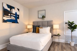 Un dormitorio moderno con una cama, lámparas de noche, una mesita de noche, una planta en maceta y un cuadro en la pared.