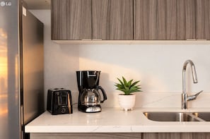 Una cocina moderna con un refrigerador de acero inoxidable, una cafetera negra, un tostador y un lavamanos con un grifo moderno.