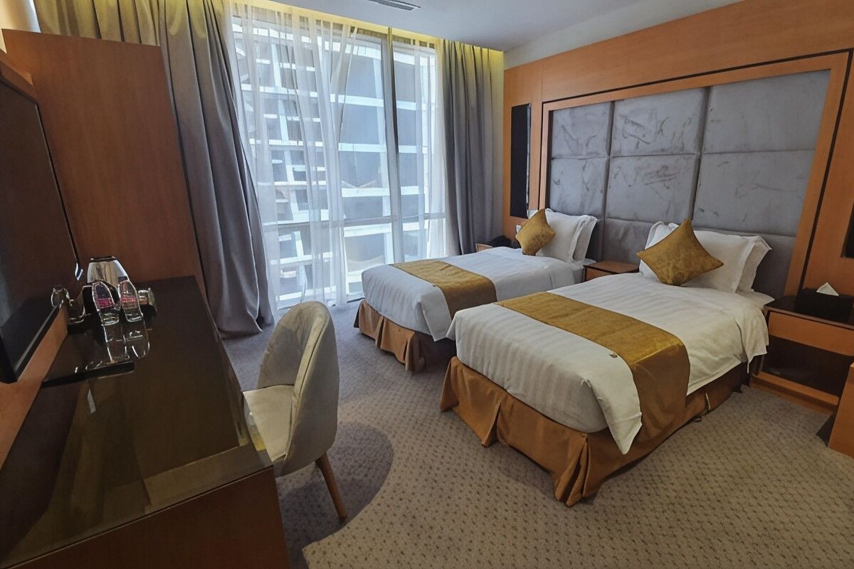 A hotel room with two beds, a desk, a chair, and a large window with curtains.