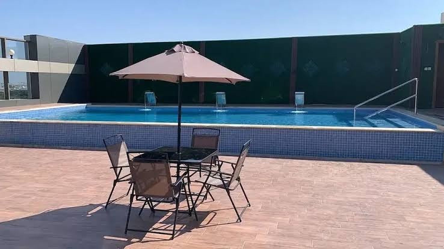 Un espace extérieur avec une piscine, une table et des chaises, un parasol et une vue sur la piscine.