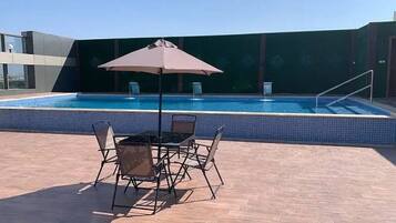 Un espace extérieur avec une piscine, une table et des chaises, un parasol et une vue sur la piscine.