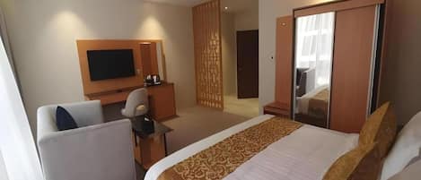 Una habitación de hotel con una cama, un escritorio, una silla, un televisor y un armario.