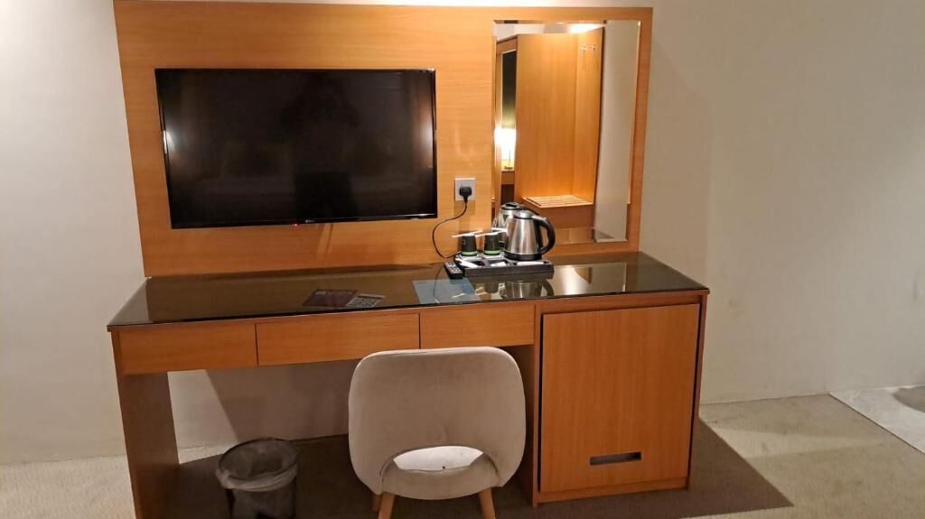 Habitación de hotel con un escritorio de madera, televisión, espejo, silla y un pequeño cubo de basura.