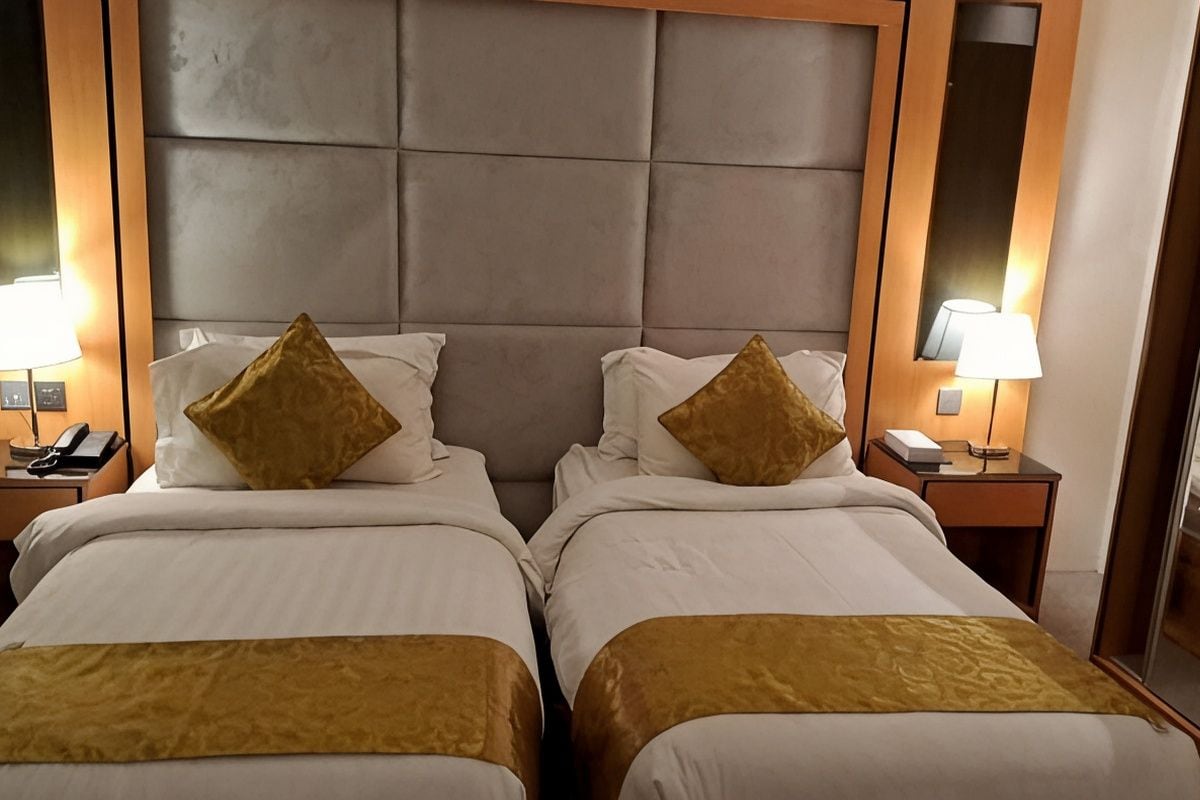 A hotel room with two beds, each with a headboard, bedside tables, lamps, and a mirror.