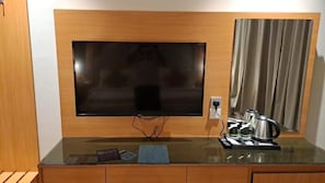 A flat-screen TV mounted on a wooden wall above a glass table with a coffee maker and a wallet. - Al Rayyan Tower (Jeddah)