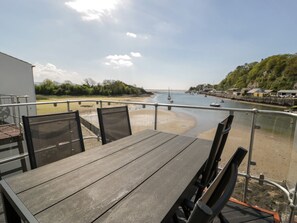 A wooden table and chairs on a balcony overlooking a beach with boats and a clear sky. - Seafarer's Haven (Porthmadog)