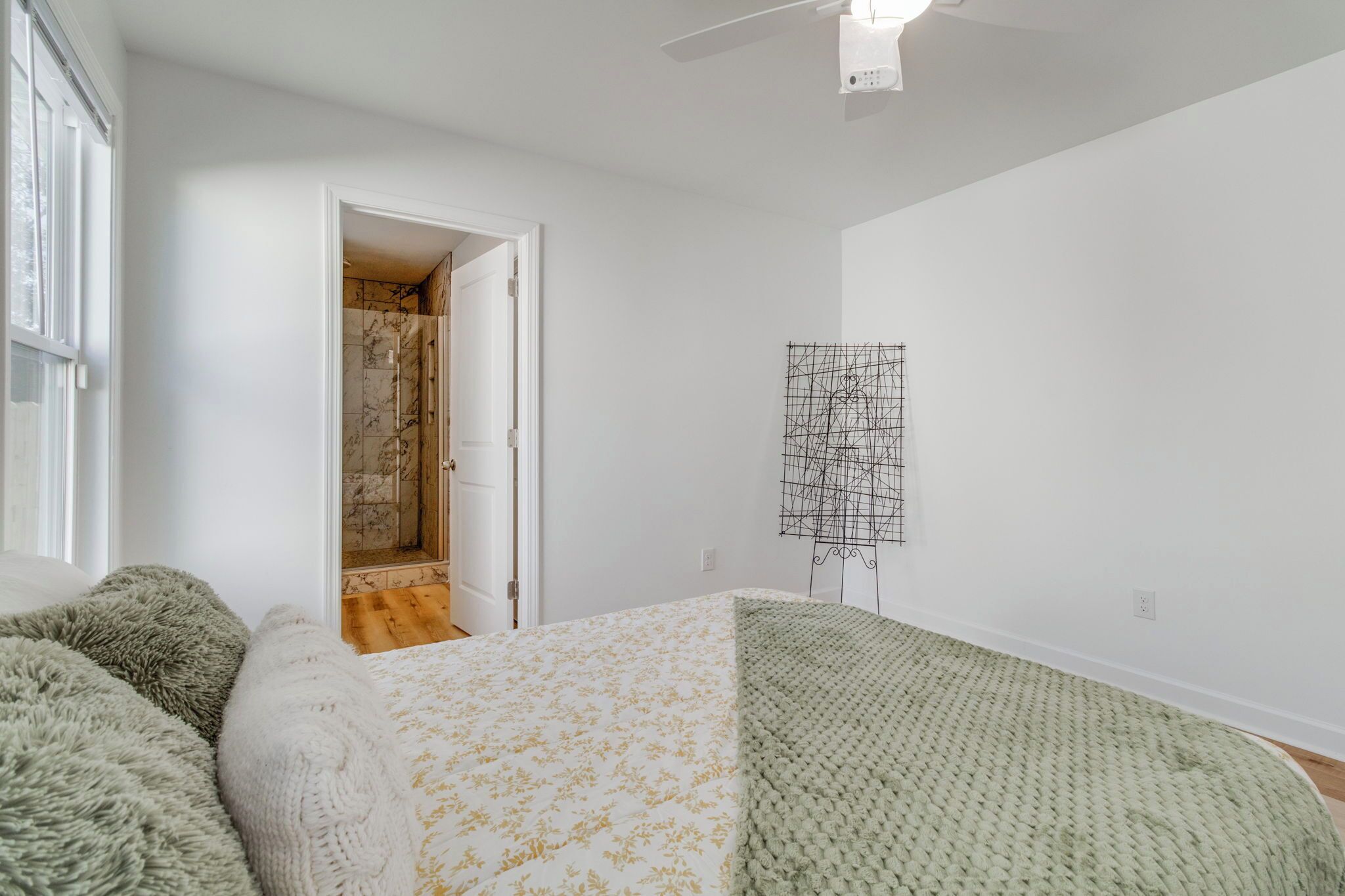 A bedroom with a bed, a door leading to a bathroom, a ceiling fan, and a wall-mounted artwork.