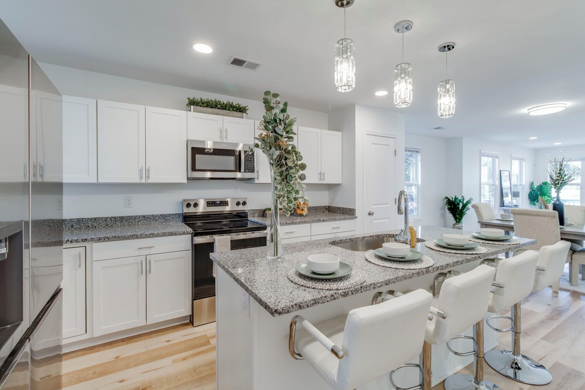 A modern kitchen with white cabinets, stainless steel appliances, a granite countertop, and a bar area with white bar stools.