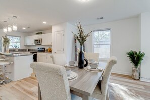 A modern kitchen with white cabinets, a microwave, and a dining area with a wooden table and patterned chairs. - 3-bedroom house in beautiful Sumter with cool AC breeze (Sumter)