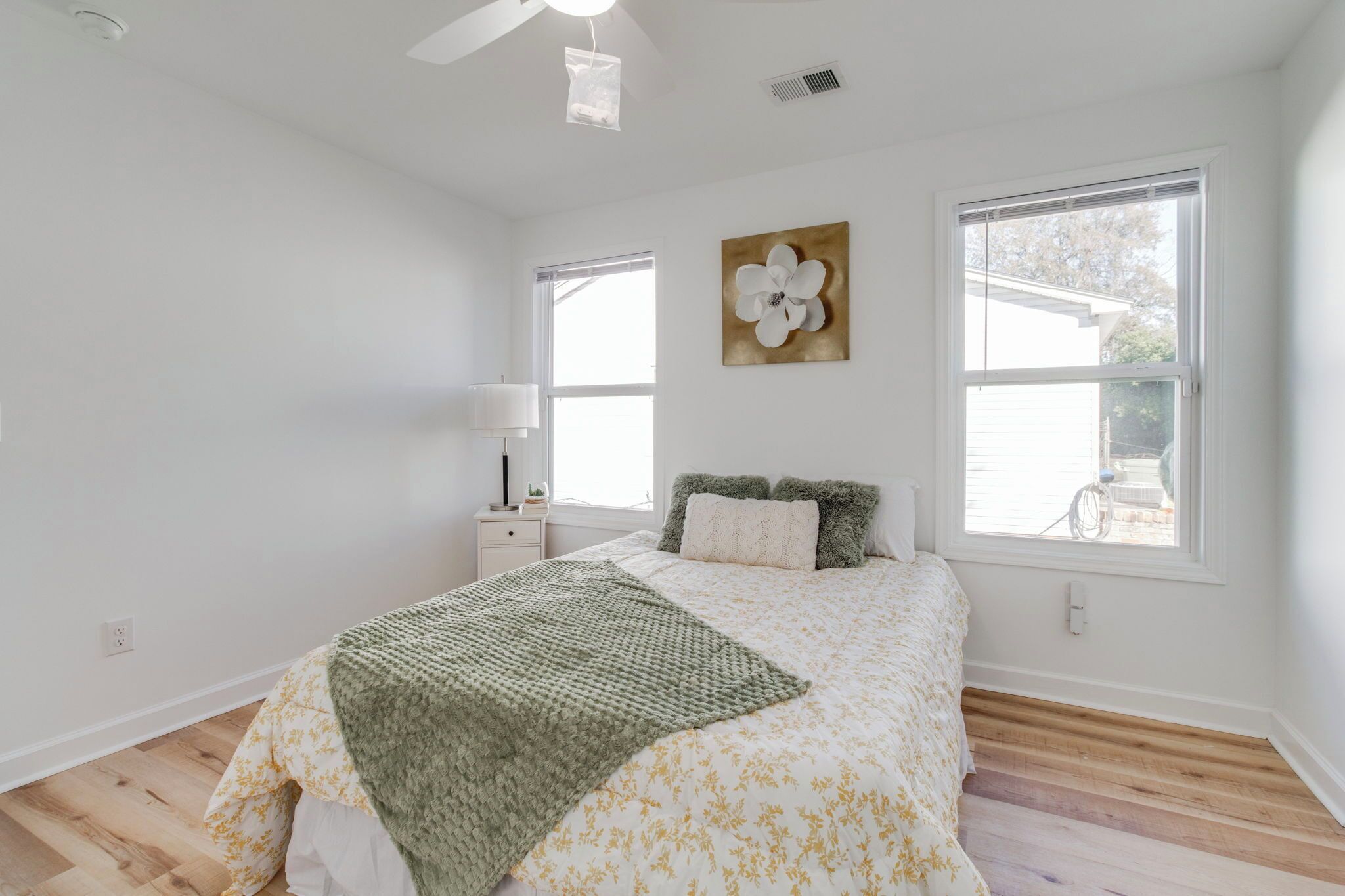 A bedroom with a bed, a nightstand, a lamp, a window, and a wall art piece.