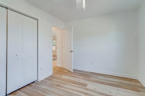 A hallway with wooden flooring, white walls, and a door leading to another room. - 3-bedroom house in beautiful Sumter with cool AC breeze (Sumter)