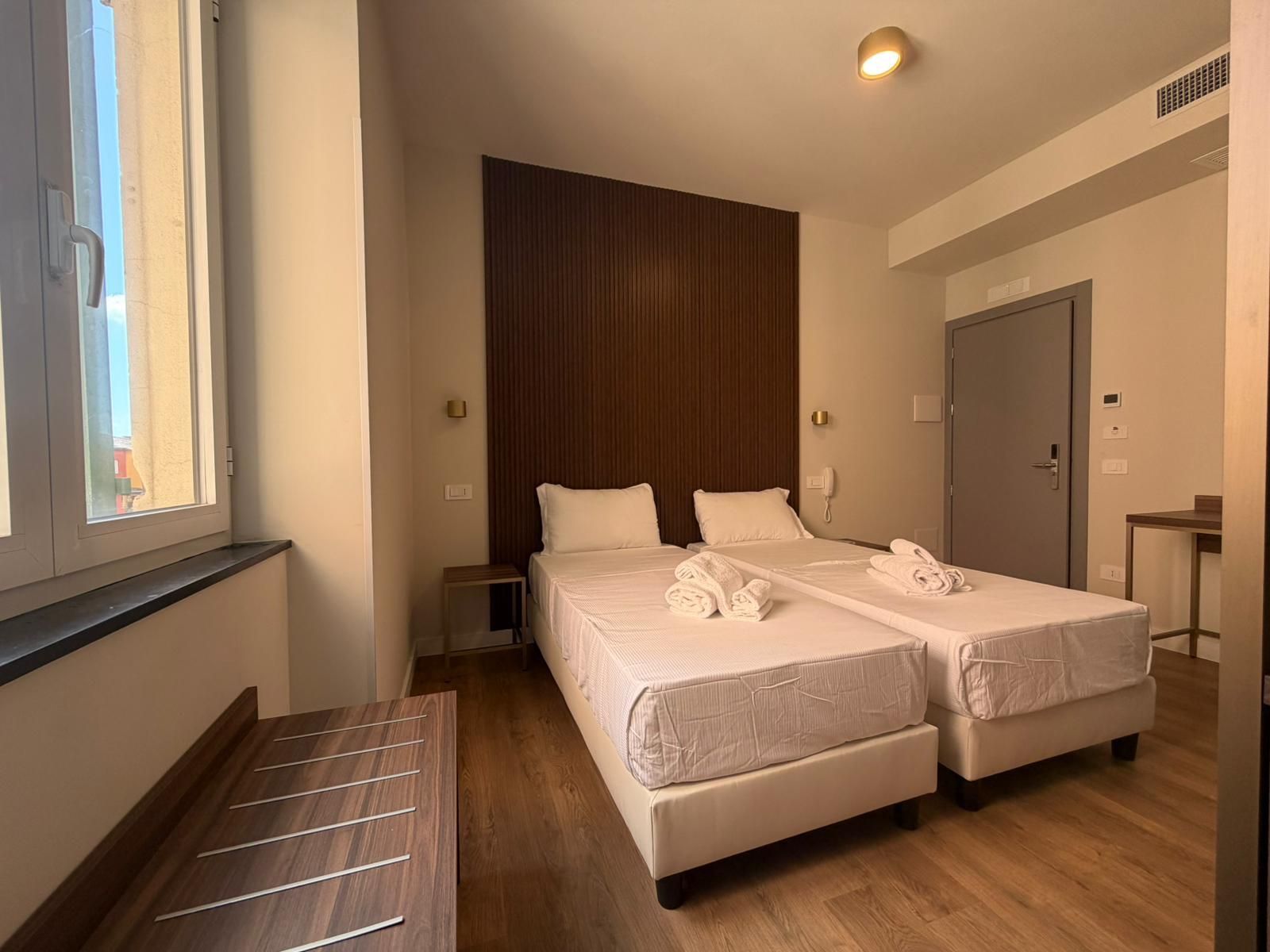 Habitación de hotel con dos camas, un banco de madera, un escritorio y una puerta.