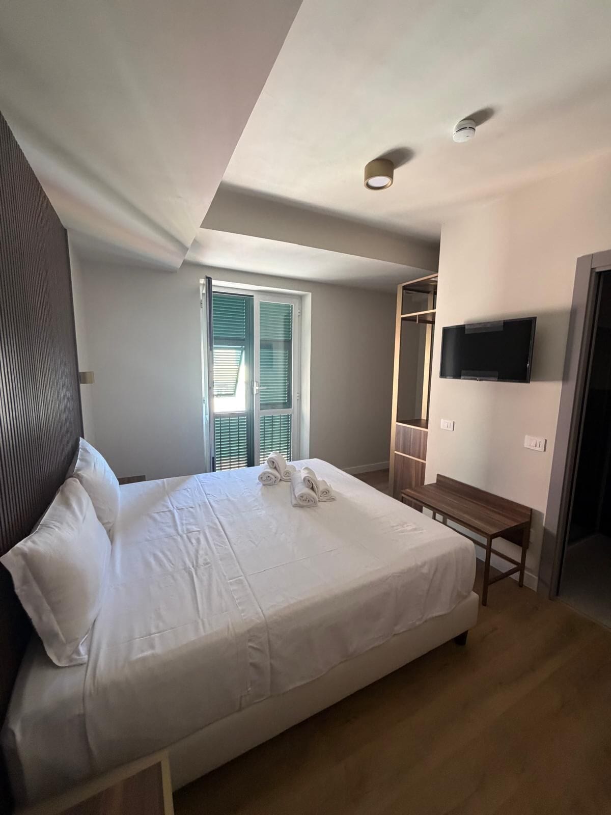 Une chambre à coucher avec un lit, un banc, une télévision et une fenêtre avec des stores.