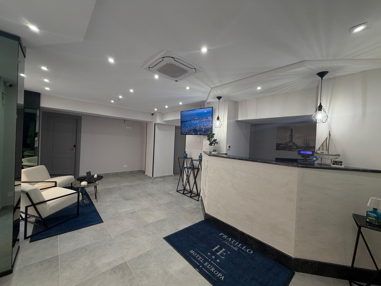 Uma área de recepção de hotel com televisão de tela plana, balcão de atendimento e sala de espera com cadeiras e uma mesa pequena.