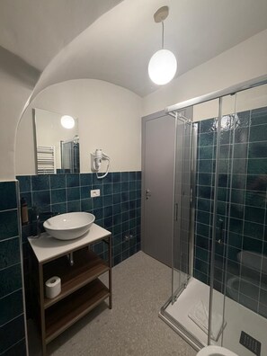 Un baño con un espejo grande, lavamanos, cabina de ducha y retrete.