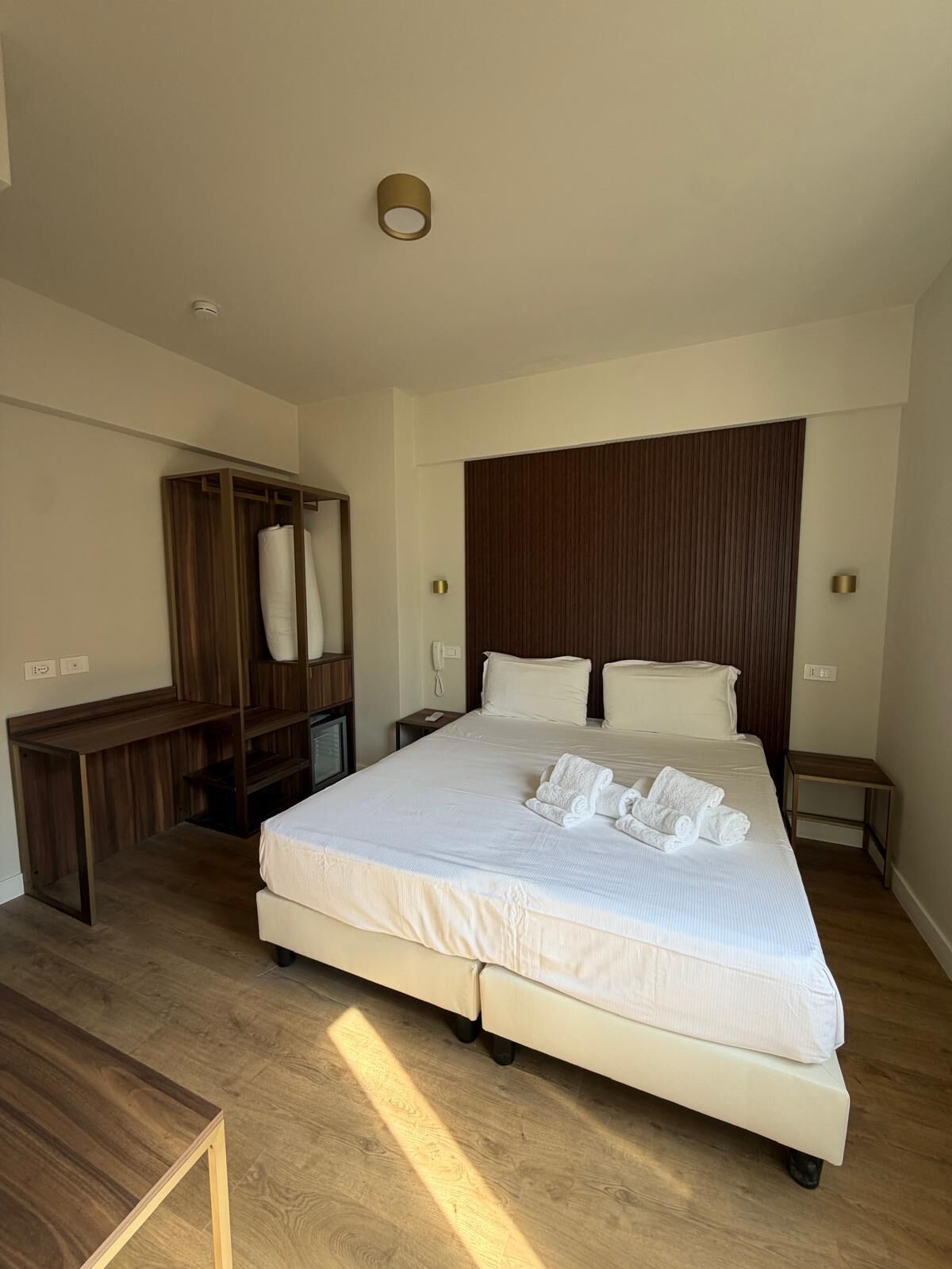 Une chambre d’hôtel avec un grand lit, une armoire en bois, un bureau et une petite table.