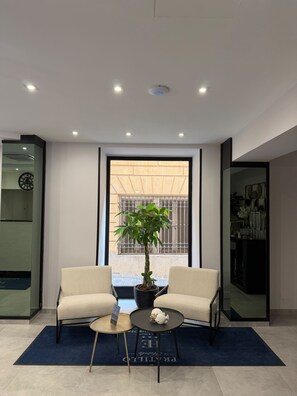 A modern interior with two armchairs, a small round table, a potted plant, and a view through a large window. - Hotel Europa (Genoa)