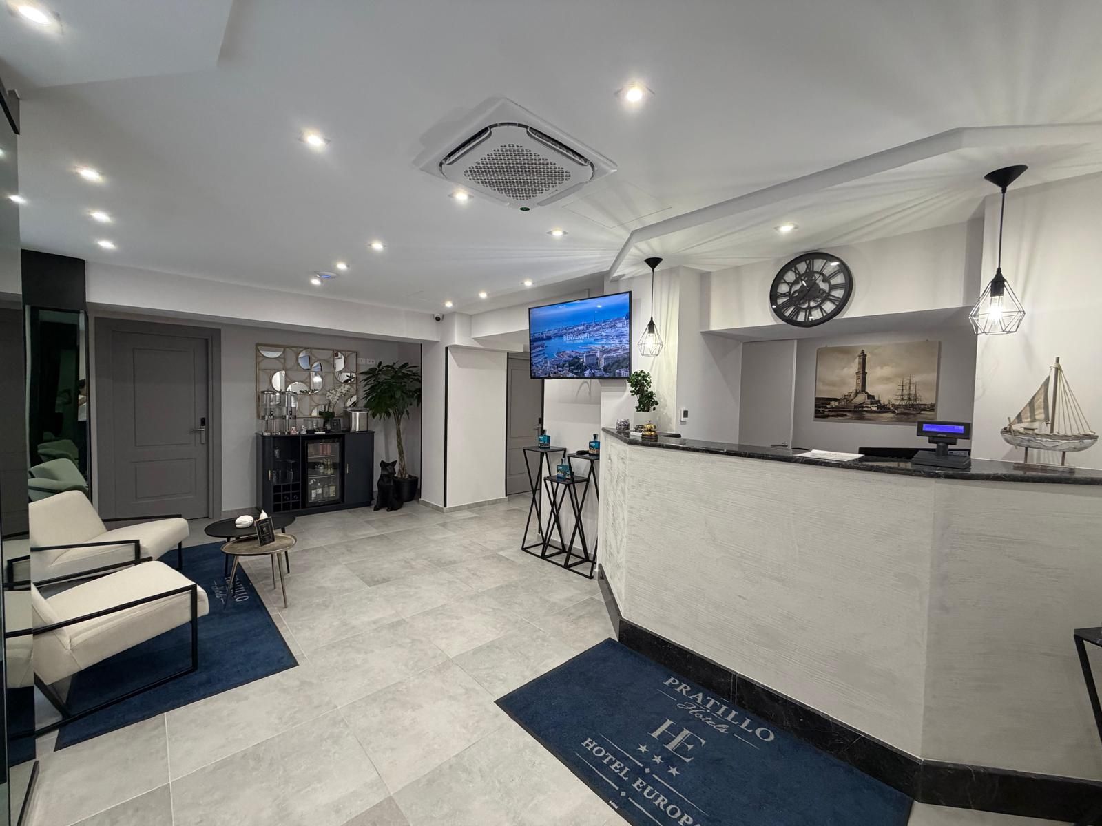 Un'area reception di un hotel dal design moderno, con una scrivania, un'area salotto e uno schermo televisivo che mostra una veduta sulla città.