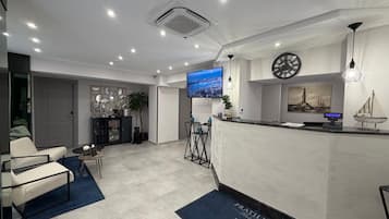 Un'area reception di un hotel dal design moderno, con una scrivania, un'area salotto e uno schermo televisivo che mostra una veduta sulla città.