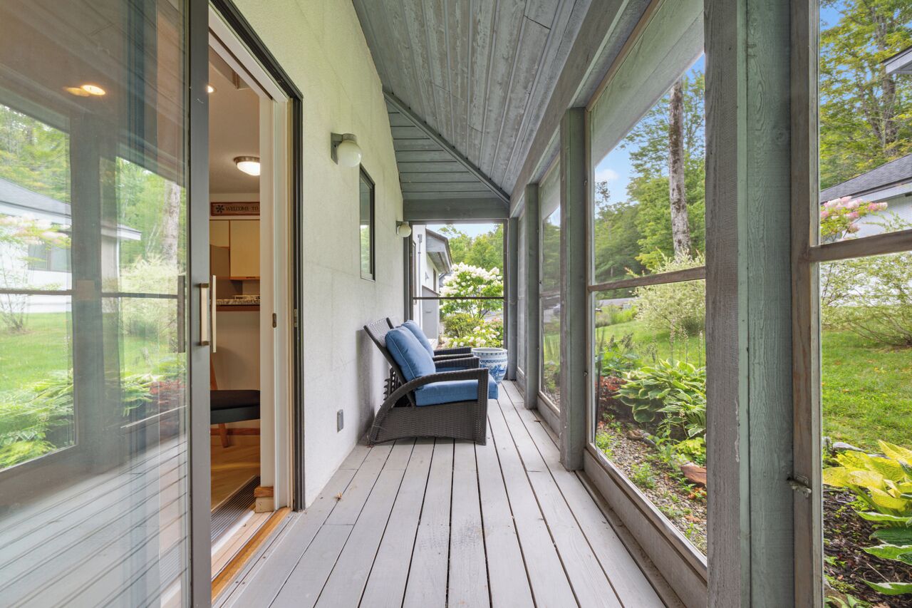 Un porche cubierto con un patio de cristal corredizo que da a una habitación, una zona de estar con sillas y vistas a un jardín.