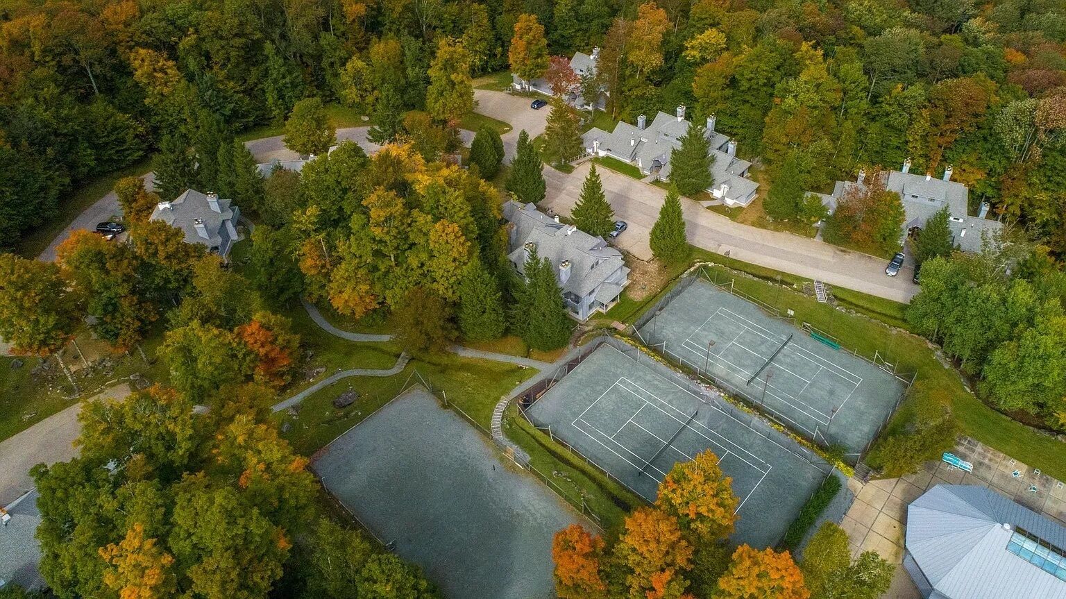 Eine Vogelperspektive zeigt eine Wohngegend mit mehreren Häusern, einem Tennisplatz und umliegenden Bäumen.