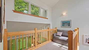 A room with a wooden railing, a grey sofa, a framed picture on the wall, and a window overlooking a green garden.