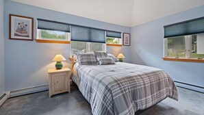 A bedroom with a bed, two bedside lamps, a nightstand, and a window with blinds. - The Woods Killington - 2B with Spa, Pool & Jacuzzi (Killington)