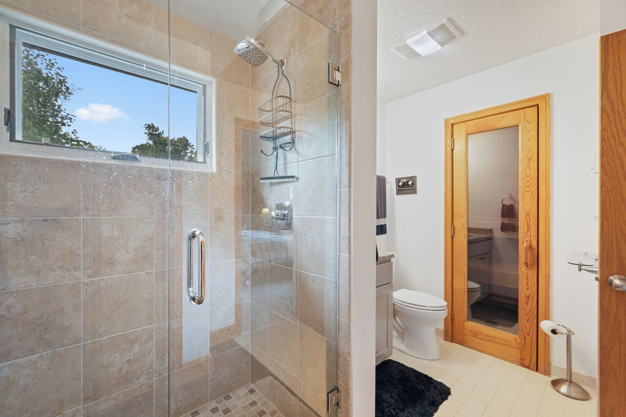 A bathroom with a glass shower enclosure, a toilet, and a wooden door.