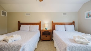 Una camera d'albergo con due letti, una ventola a soffitto, un comodino con una lampada e un quadro appeso al muro.