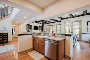 A modern kitchen with a central island, wooden cabinets, and a stainless steel dishwasher. - Chandler Cottage, Charming Golf Cottage in Hampton Hall (Bluffton)