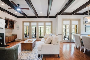 A spacious living room with a fireplace, a sofa, a coffee table, and a dining area with chairs. - Chandler Cottage, Charming Golf Cottage in Hampton Hall (Bluffton)