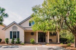 A two-story building with a covered porch, a small front garden, and a parking lot. - Chandler Cottage, Charming Golf Cottage in Hampton Hall (Bluffton)