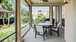 Una veranda coperta con tavolo e sedie, una ventola a soffitto e vista su una zona residenziale.