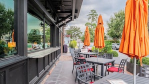 An outdoor seating area with tables and chairs, covered by orange umbrellas, and a view of the street. - Lowcountry Landing! 3-story Townhouse in Old Town's Promenade (Bluffton)