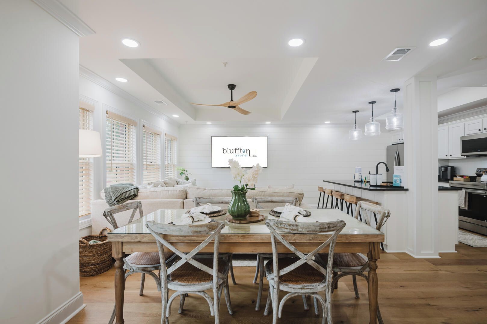 Una cocina moderna con armarios blancos, un comedor con mesa y sillas de madera y un ventilador de techo.