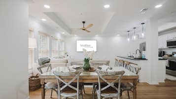 A modern kitchen with white cabinetry, a dining area with a wooden table and chairs, and a ceiling fan.