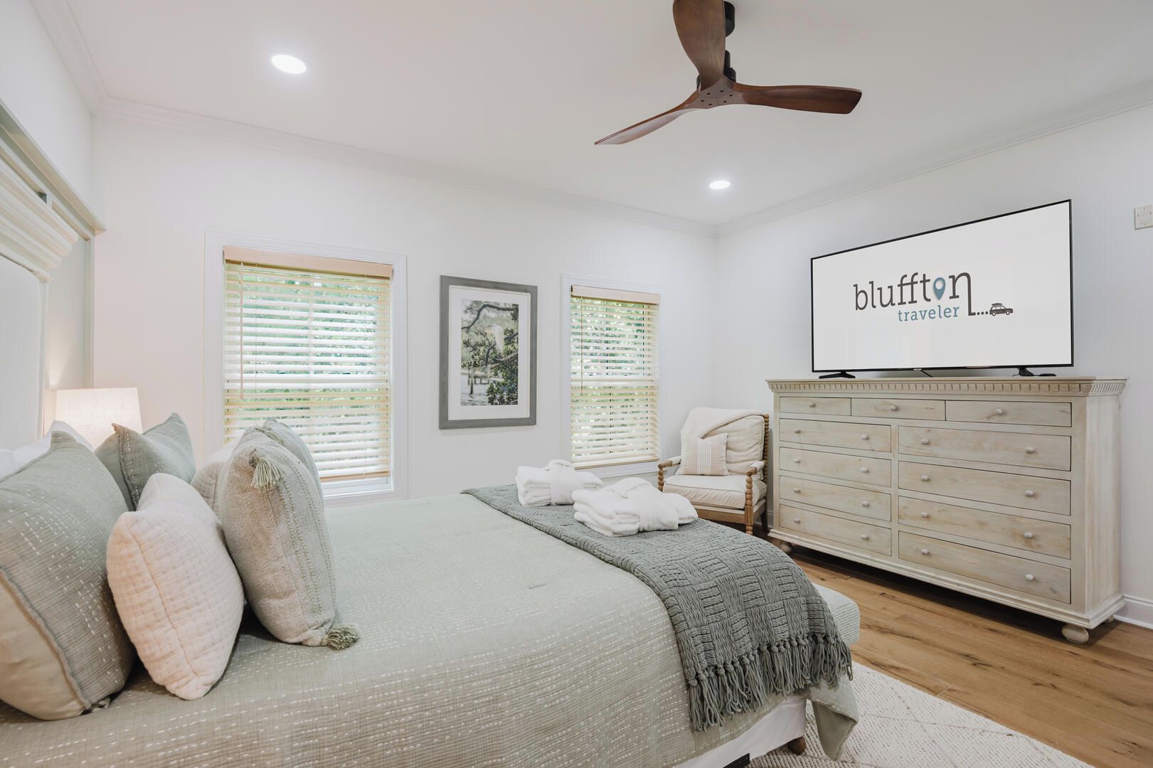Une chambre à coucher comprenant un lit, une commode, un ventilateur de plafond et un téléviseur fixé au mur.