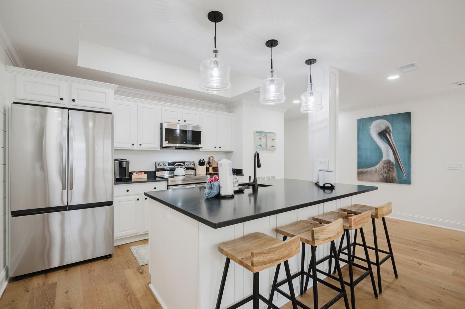 A modern kitchen with white cabinetry, stainless steel appliances, and a central island with bar stools.