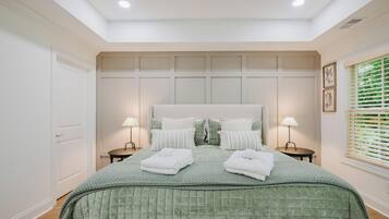 A bedroom with a large bed, two bedside tables, and a window with blinds.