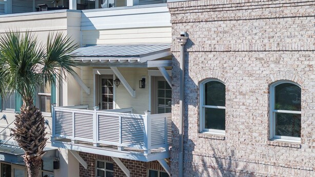Ein zweistöckiges Gebäude mit Balkon, Ziegelverkleidung und einer Palme.