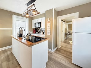 A modern kitchen with a central island, white cabinetry, a stainless steel kettle, and a hanging light fixture. - Cedar Point in 10 Min  Cozy 2BR (Sandusky)