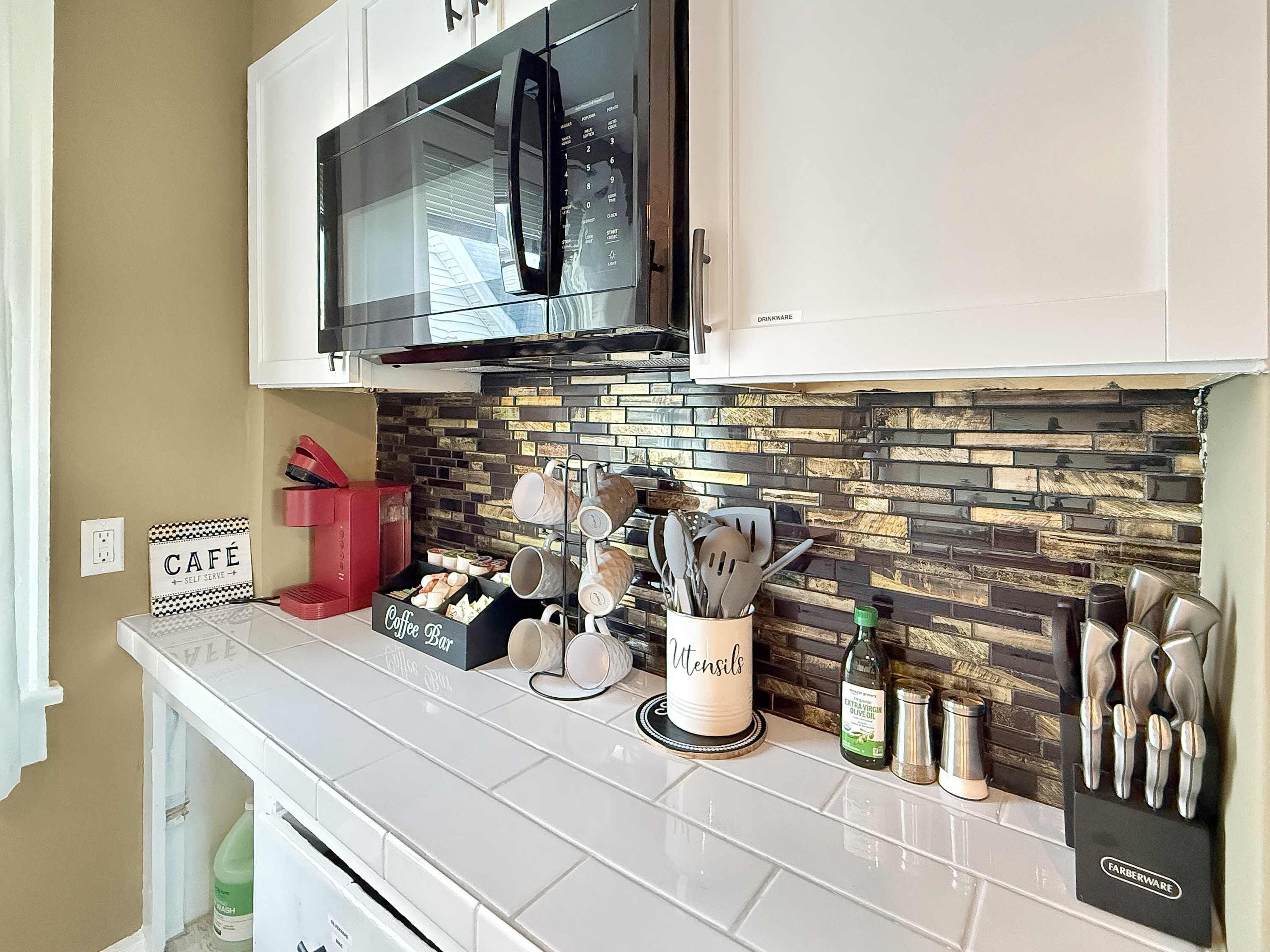 A kitchen with a microwave, coffee bar, utensils holder, and a sign that says 'Café Self Serve'.