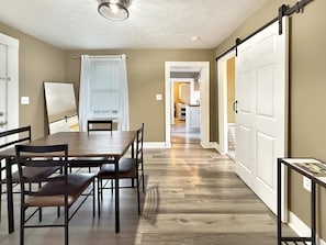 A dining area with a wooden table and chairs, a sliding door, and a view into a kitchen. - Cedar Point in 10 Min  Cozy 2BR (Sandusky)