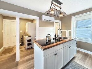 A kitchen with a wooden countertop, white cabinets, a black faucet, and a window with blinds. - Cedar Point in 10 Min  Cozy 2BR (Sandusky)