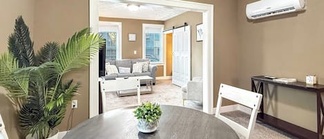 A room with a round table, chairs, a potted plant, a white door, and an air conditioning unit.